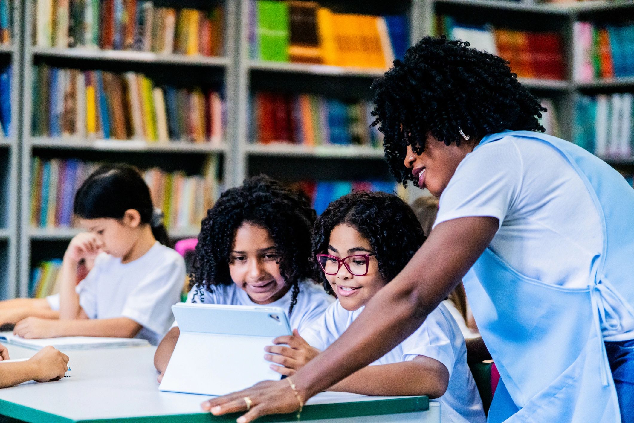Teacher helping children of African descent learn using a digital tablet in a school library